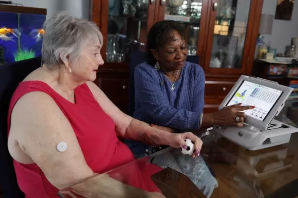 Elderly veteran using a therapy tablet with caregiver support in a home environment
